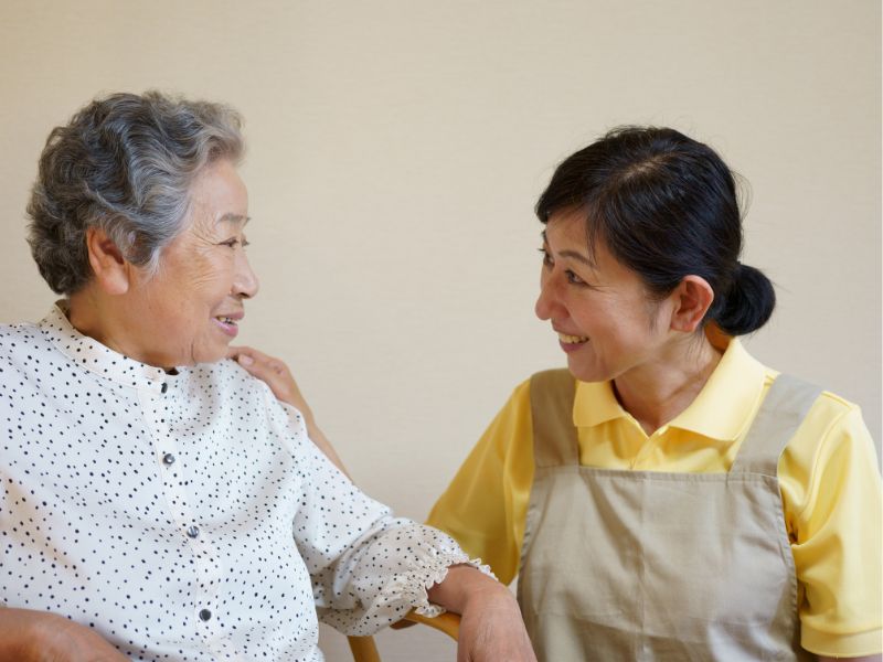 高齢者と中年の女性介護士が微笑みながら見つめ合っている様子のイメージ