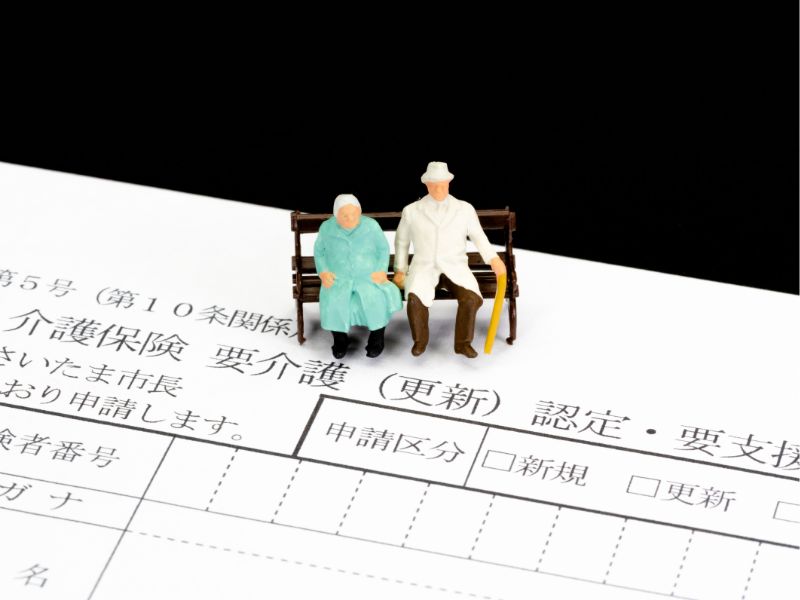 介護保険の要介護・支援申請書の上にベンチに座った老夫婦の人形が置かれているイメージ