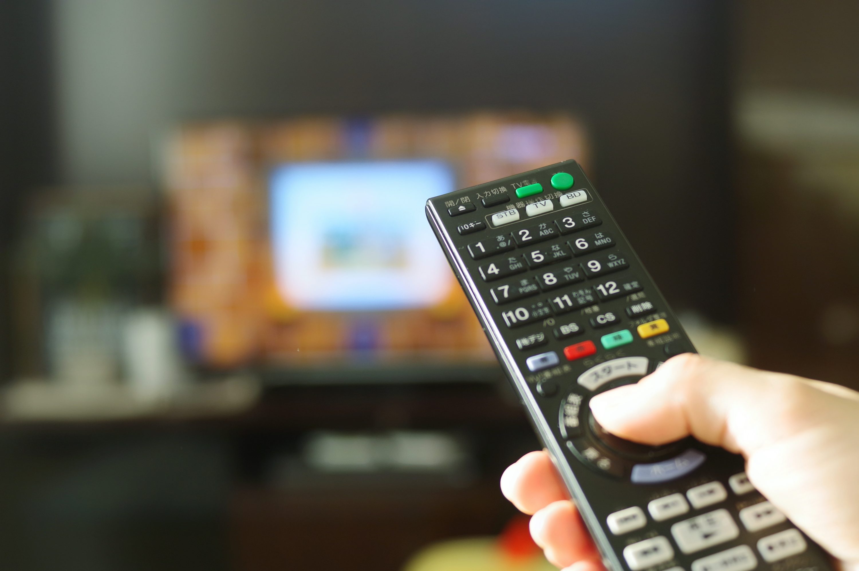 テレビに向かってリモコンボタンを押している手元のイメージ