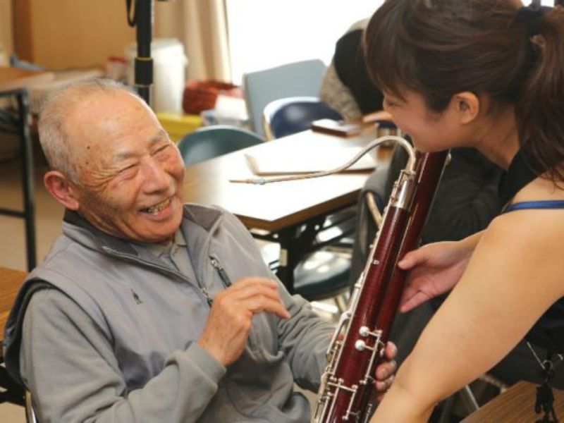 笑顔のお年寄りに管楽器を渡す女性の画像