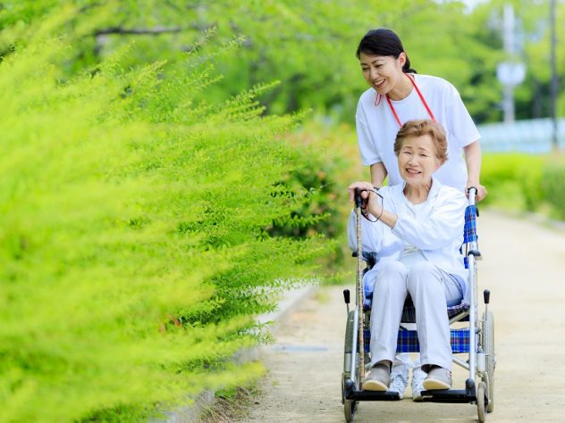高齢女性の座る車椅子を押す女性介護スタッフ