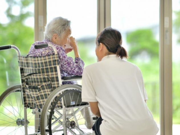 車椅子の高齢女性に寄り添って話をする女性スタッフ