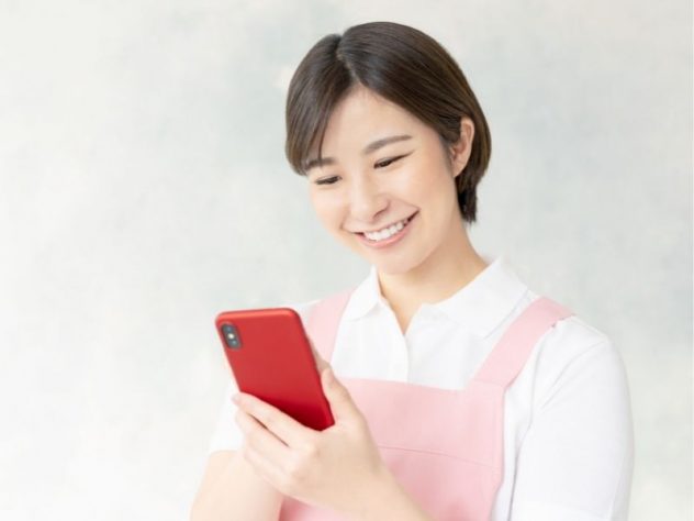 スマートフォンを操作する女性介護士の画像