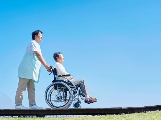 高齢女性の車椅子を押す男性介護士の画像