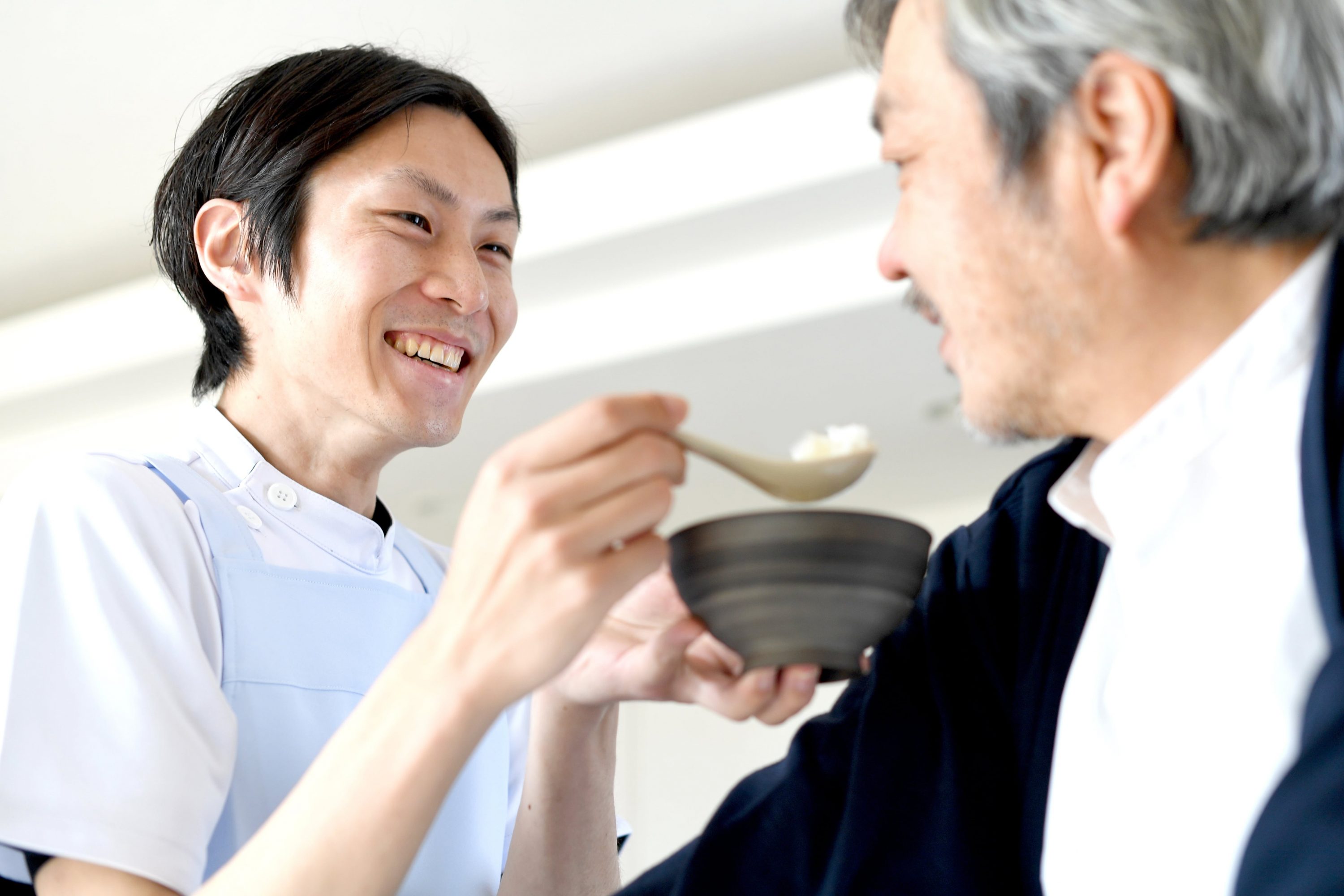 男性介護士がスプーンでご飯を中年男性に食べさせているイメージ