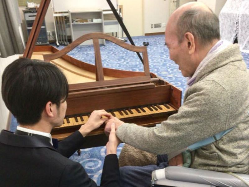 ピアノの鍵盤にお年寄りの手を持っていき支える男性の画像