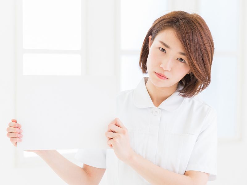 困った表情で真っ白な画用紙を掲げている介護士のイメージ