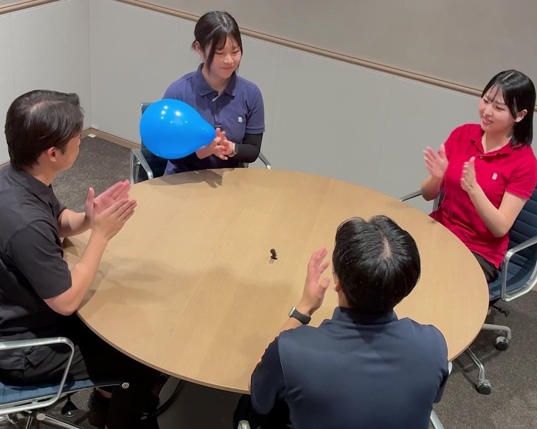 円卓を囲んだ4人のうち、一人が青い風船を持っている画像