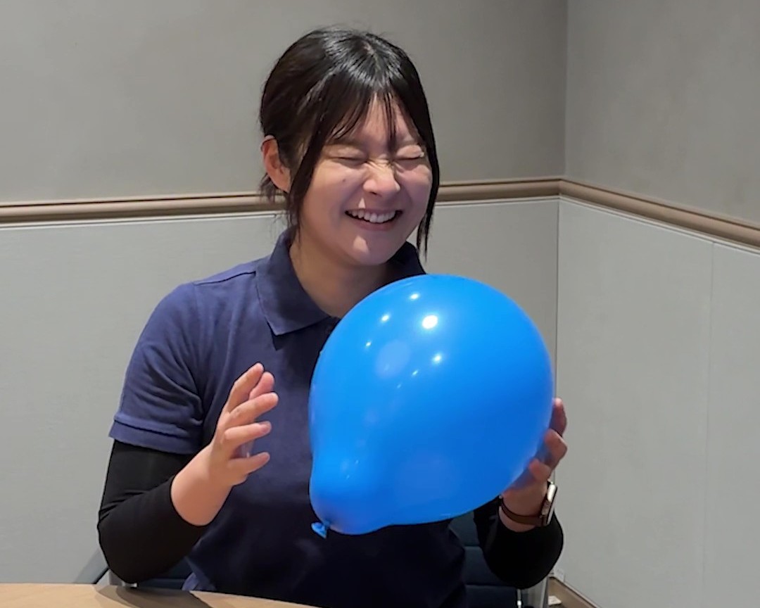 女性が目をつむり笑顔で青い風船を持っている画像