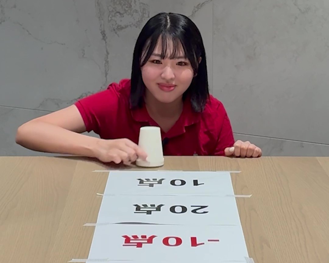 点数が書かれた紙に向かって紙コップを滑らせようとしている女性の画像