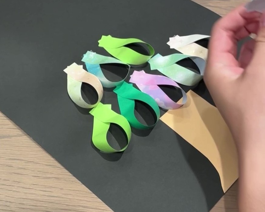 作ったわっかを、ツリーの形になるように黒の画用紙に貼り付けている様子